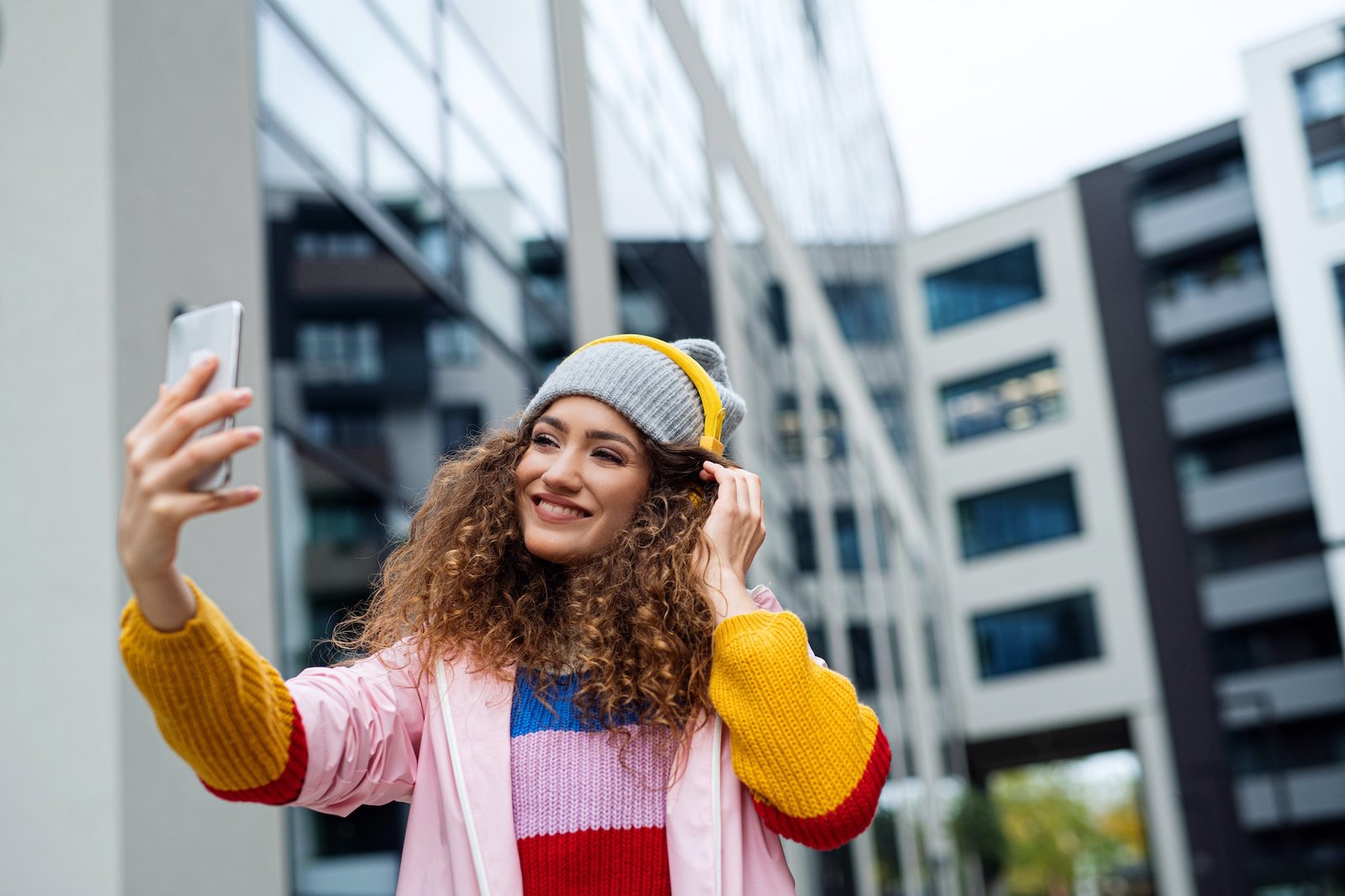Young woman with smartphone making video outdoors on street, tik tok concept.